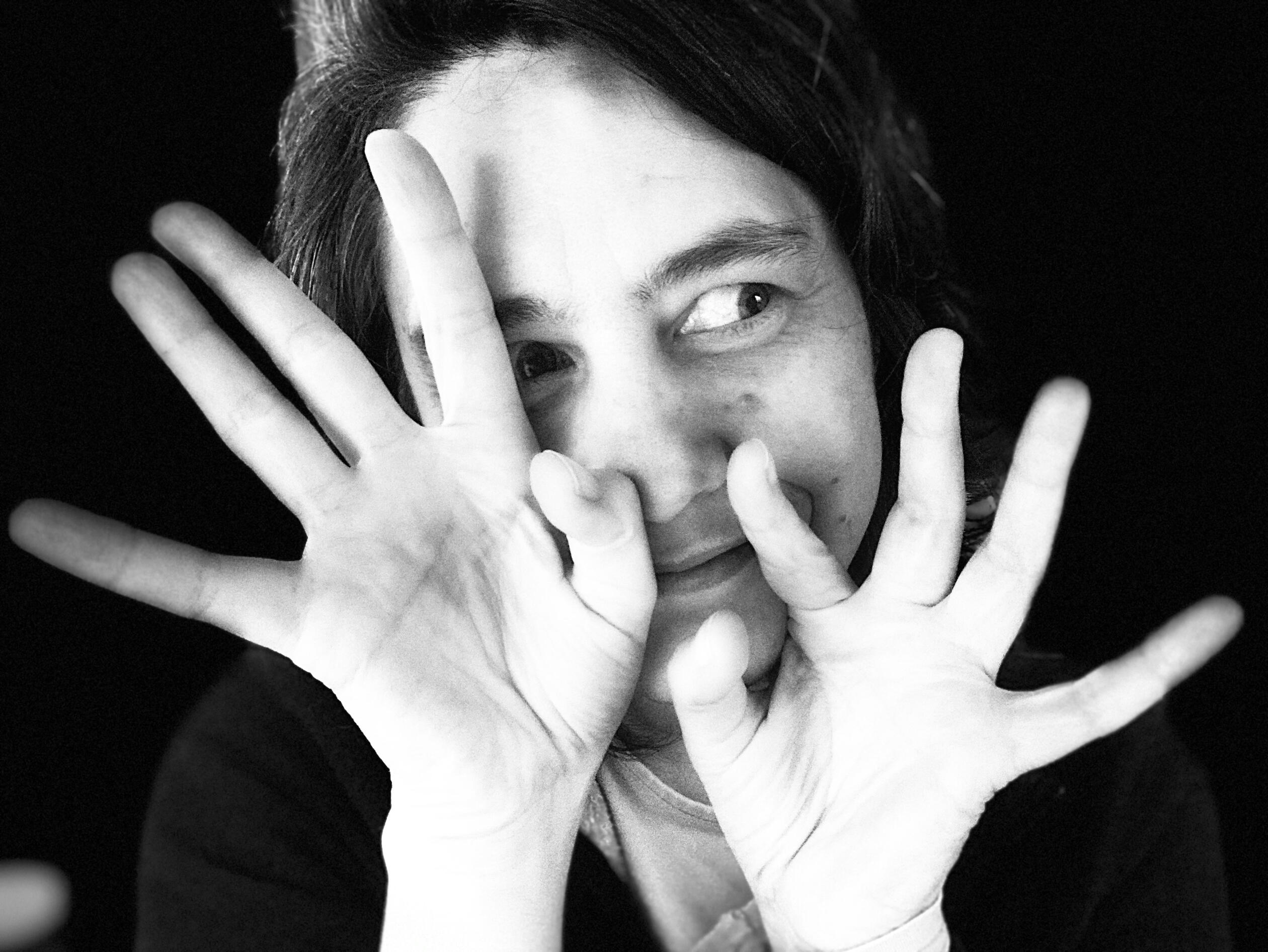 Black and white self-portrait, white woman looking playfully off to the side with hands partly securing the face, palms out and fingers open.