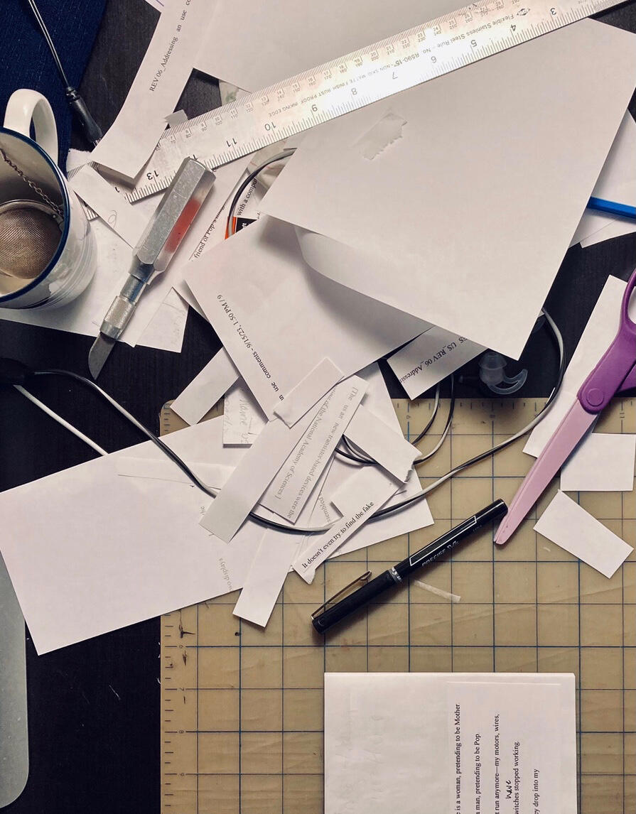 Color photograph, overhead view of a black table top with scattered paper scraps, X-Acto knife, scissors, and other supplies for making a picture book a dummy.