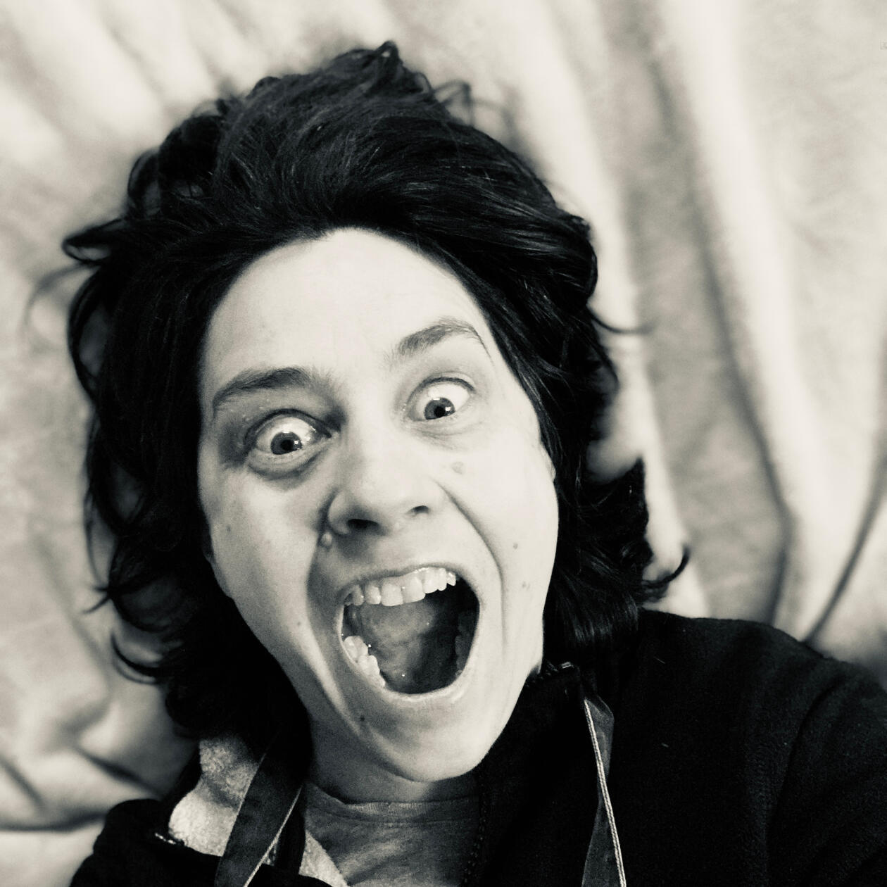 Last image in grid of self-portraits. Black and white photograph: Headshot dramatic look of surprise, eyes and mouth wide open. Taken from above lying down, so that hair is spread around as if surprised too.